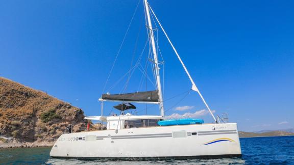 Der luxuriöse Lagoon 560 Katamaran mit eleganten Linien gleitet sanft über das türkisfarbene Wasser vor der felsigen Küs